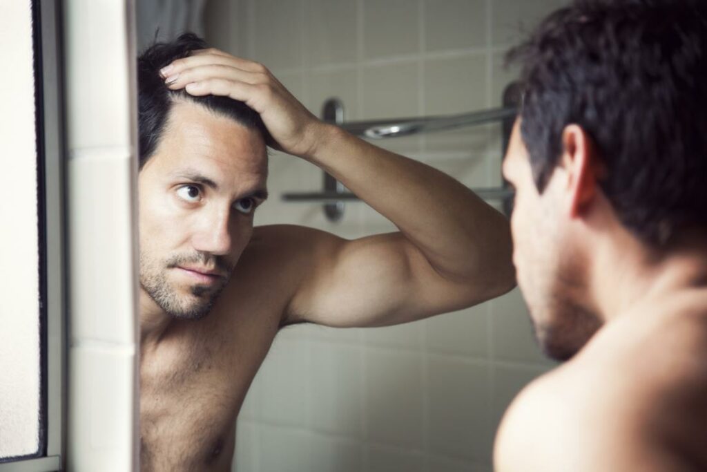man wondering if masturbation causes hair loss looking at hairline in bathroom mirror